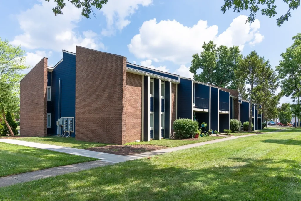 Freshly painted apartment complex featuring dark blue siding contrasted with original red brick exterior walls, white trim, and landscaped greenery on a sunny day.
