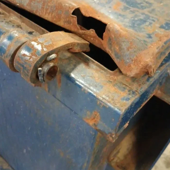 Rusted and broken metal hinge on a container before repair, showing corrosion and structural damage.