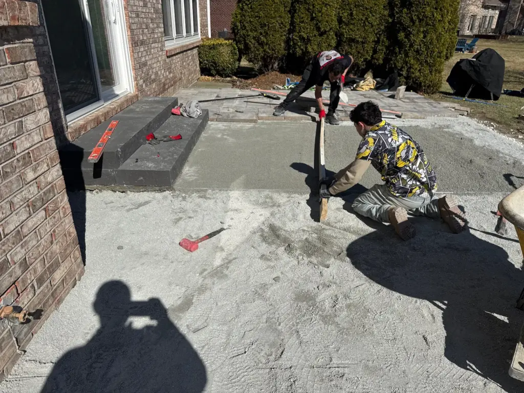 Hardscaping patio installation in progress at a home in Carmel, Indiana with workers leveling the base before paver installation.