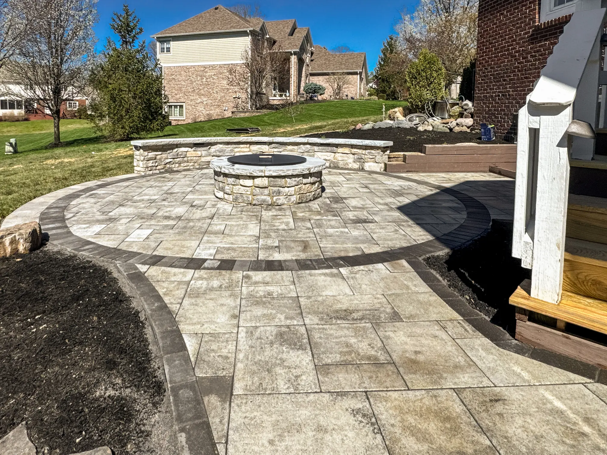 Custom paver patio installation with circular fire pit and retaining wall in Carmel, Indiana backyard