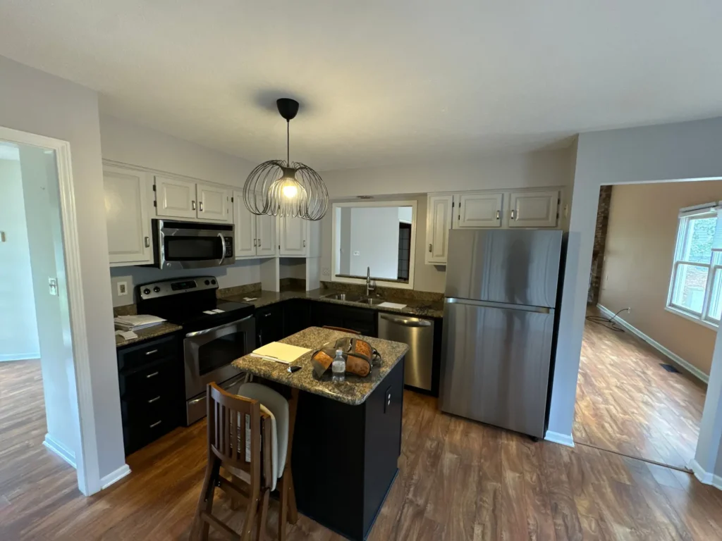 Before: Kitchen with white upper cabinets, dark lower cabinets, small island, and older layout in Indianapolis, Indiana
