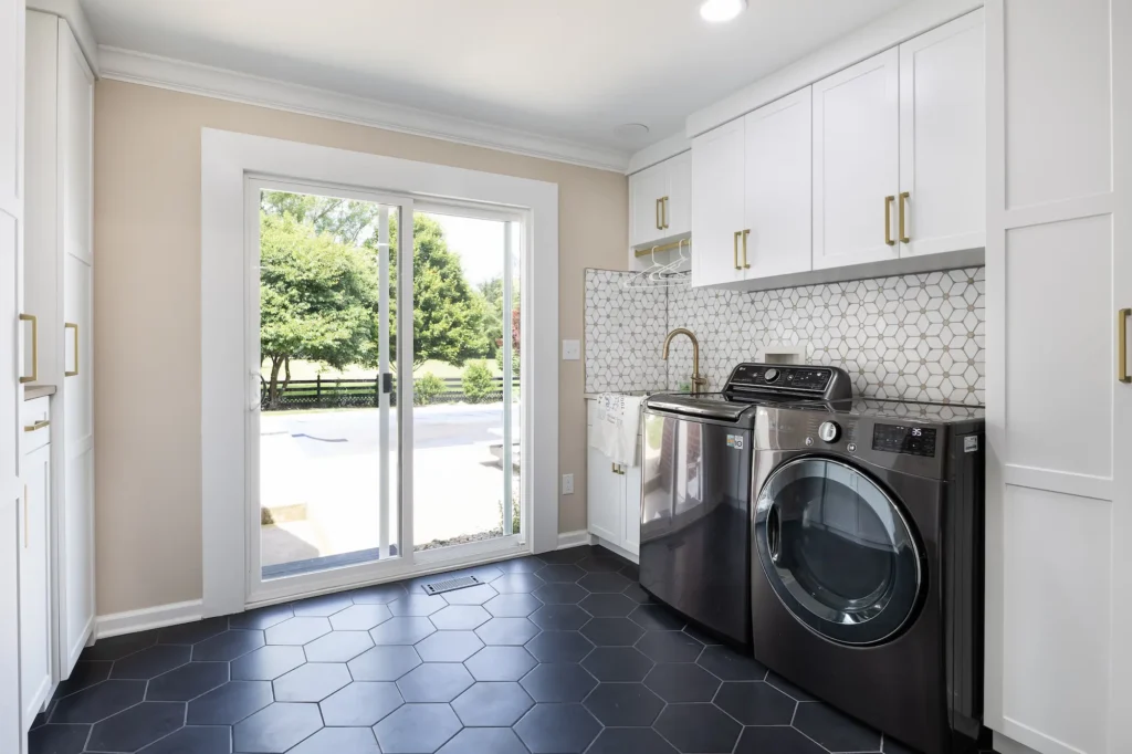 Laundry room renovation featuring black hexagon tile flooring, white cabinets, utility sink, and patio access in Carmel, Indiana