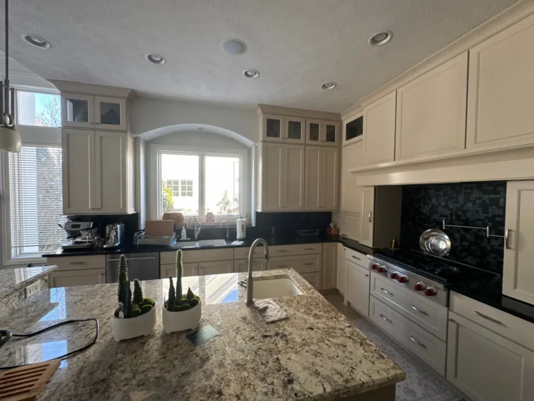 Kitchen before renovation with off-white cabinets, dark countertops and backsplash, and silver hardware