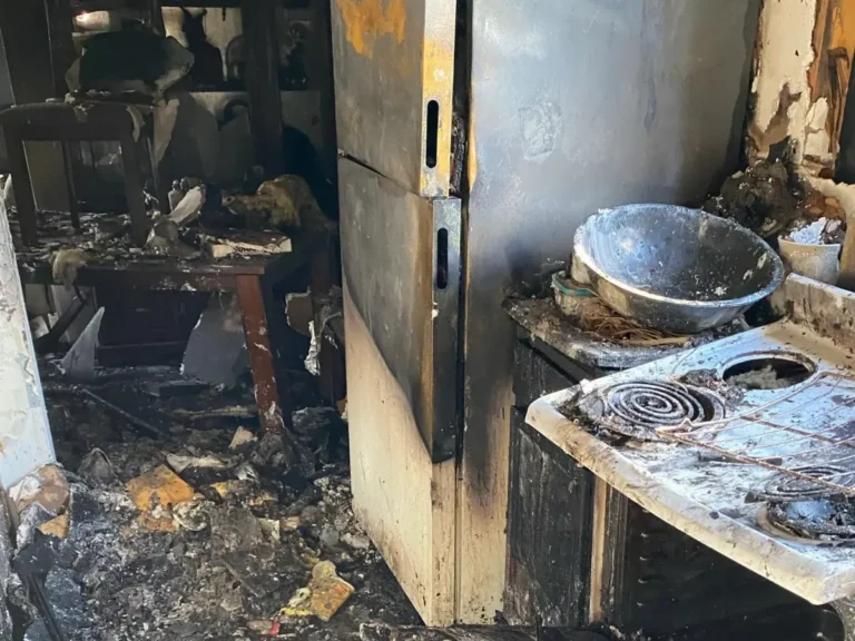 Severely burned apartment kitchen in Indianapolis, Indiana showing fire-damaged appliances, soot, debris, and water from firefighting efforts before cleanup.